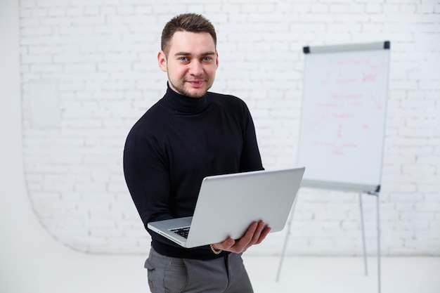 A male businessman manager smiles and stands with a laptop in his hands and looks at the screen. Stands on a white background.