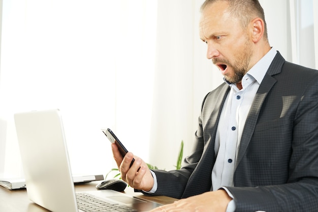 Foto un uomo d'affari maschio legge le notizie sul suo smartphone ed è scioccato e sorpreso