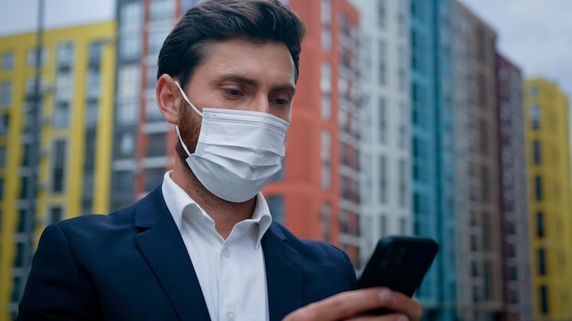 Male businessman in respiratory protection medical mask work on quarantine outdoor texting on