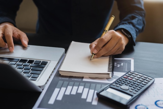 Male businessman sitting at a table at home working on a laptop and writing down ideas in a notebook