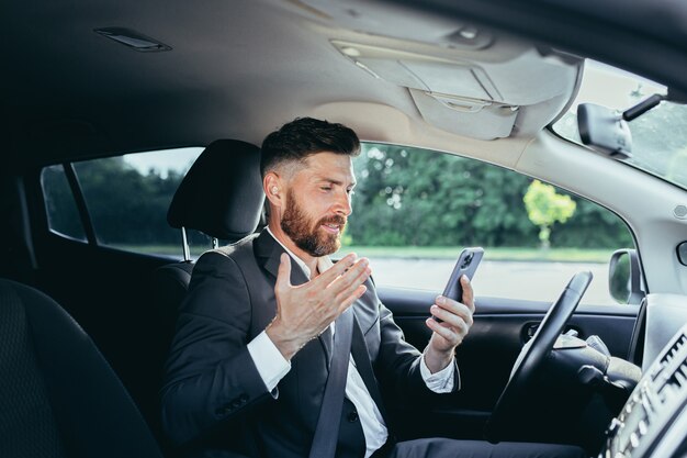 Male businessman successful rejoices and smiles reads news from mobile phone win and success meeting, man sits in car