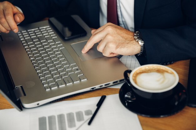 Male businessman using laptop in cafe. Notebook and coffee cup close up.