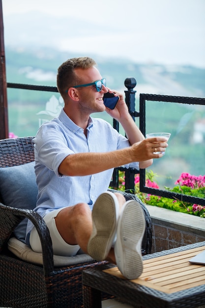 美しいパノラマの景色と休暇でラップトップに取り組んでいる男性のビジネスマン。旅行中にコーヒーを飲み、コーヒーを飲みながら電話で話す成功したマネージャー