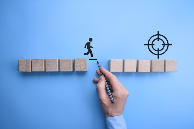 Male bussinnes man hand drawing a connecting line between two sets of wooden blocks for a silhouetted man to walk across.Conceptual of teamwork and support.