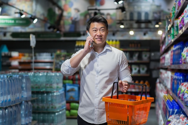 A male buyer in a supermarket chooses goods and makes purchases an asian man talks cheerfully on the