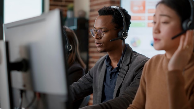 Male call center operator using headset to help people, giving telemarketing assistance to clients on helpline. Person working at customer support service office, offering advice.