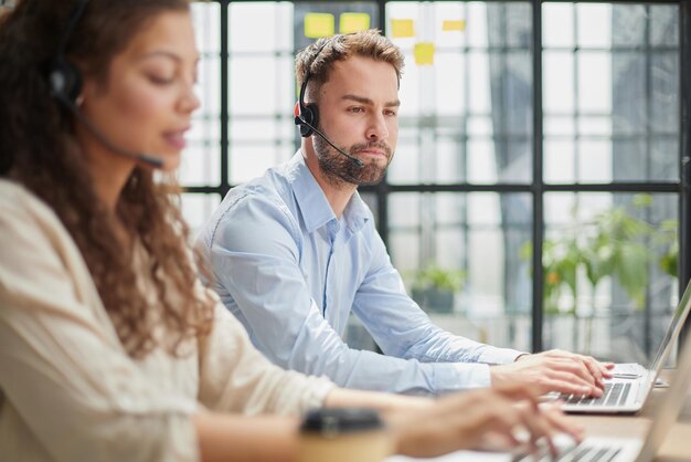 Male callcenter operator with headphones sitting at modern office