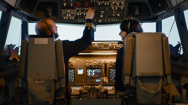 Capitano maschio che fissa i livelli di altitudine e longitudine per pilotare l'aereo, utilizzando il comando del pannello di controllo per il decollo. aviatori in volo con navigazione sul cruscotto e pulsanti sul parabrezza.