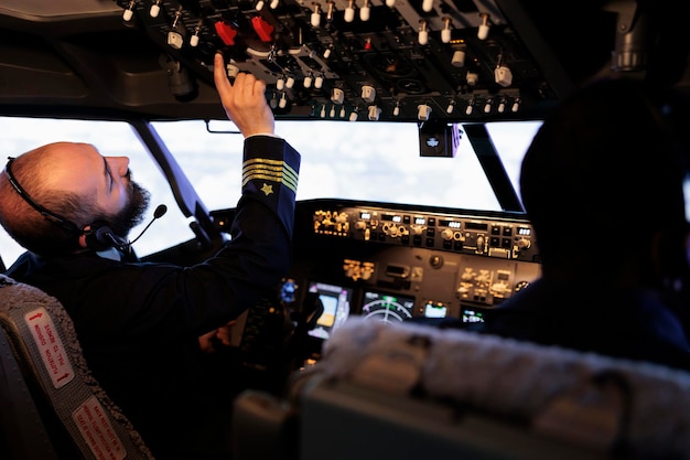 Фото Капитан-мужчина нажимает кнопки, чтобы включить управление приборной панелью, используя команду панели в кабине, чтобы управлять самолетом. летающий реактивный самолет с радиолокационным компасом и воздушной навигацией.