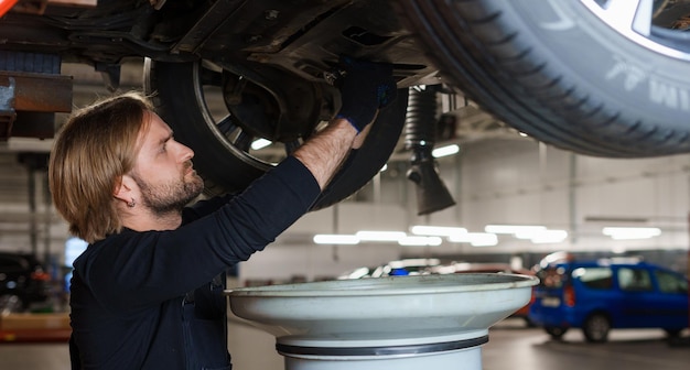 Un meccanico di auto in uniforme cambia l'olio nel motore mentre sta sotto l'auto sull'ascensore