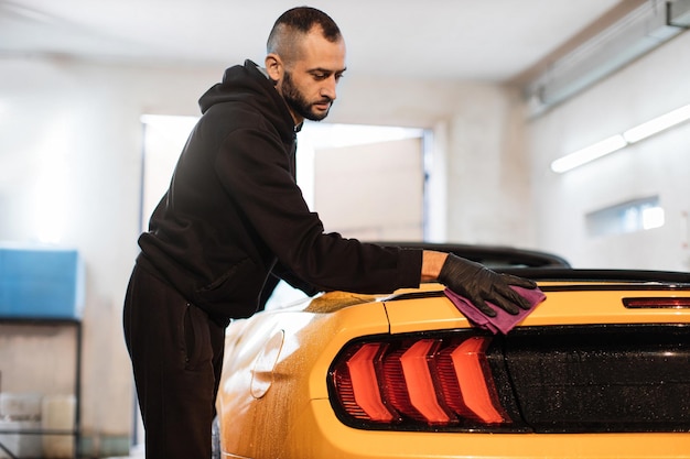 L'addetto all'autolavaggio maschio tiene in mano la microfibra e lucida l'auto di lusso sportiva gialla