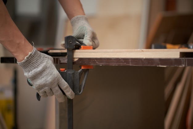 Male carpenter clamps board in vice in workshop 