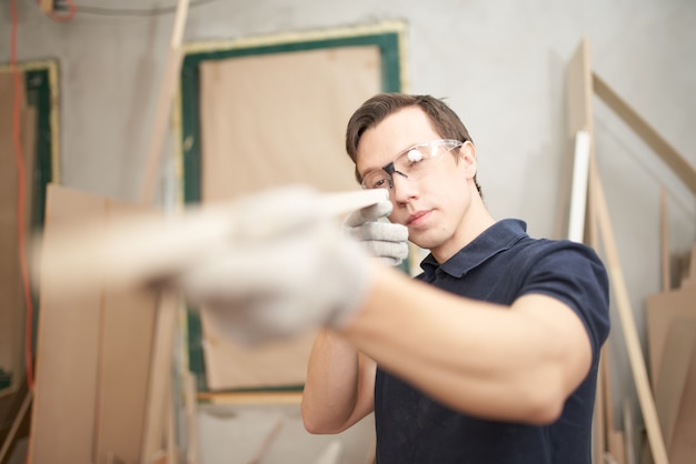 Male carpenter in glasses holds board in workshop