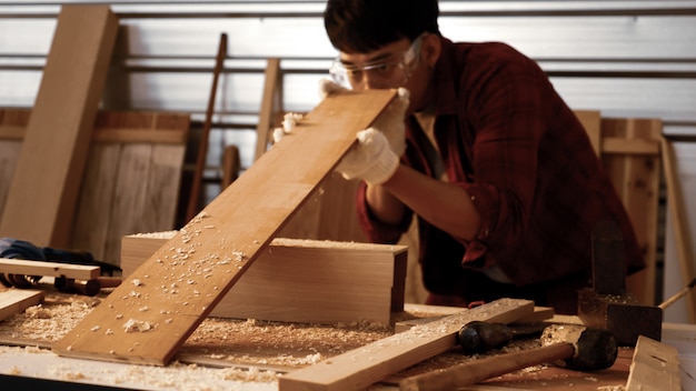 Male carpenter holding and checking piece of board at site.