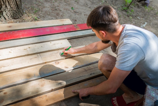 Male carpenter lays out a structure from wooden boards closeup