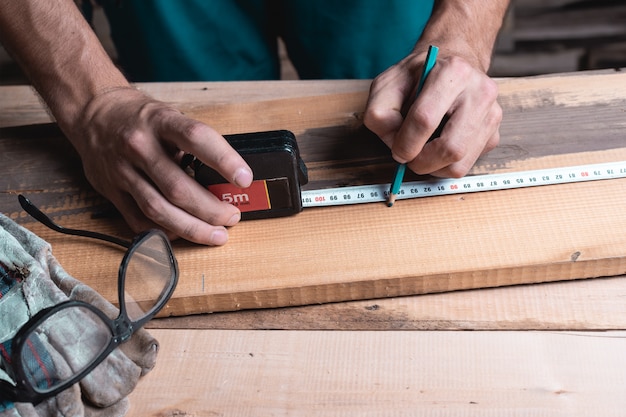 Male carpenter notes with pencil using measuring tape on the Board, marks for saw cut