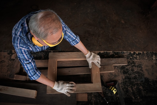 The male carpenter uses sandpaper to polish the woodwork.