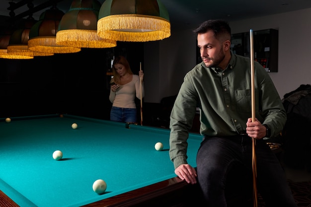 Male in casual wear sits on billiards table, looking at game, snooker sport game concept. portrait