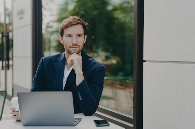 Photo male ceo with thoughtful expression browses fast wireless mobile internet works on laptop