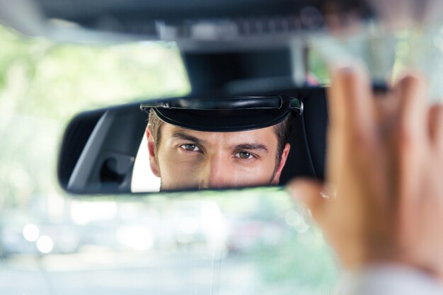 Male chauffeur sitting in a car and looking at his reflection in a mirror