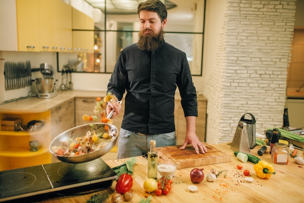 Male chef cooking meat with vetables into the pan