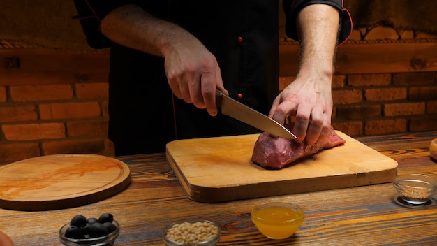 Male chef cutting  piece of beef on wooden board