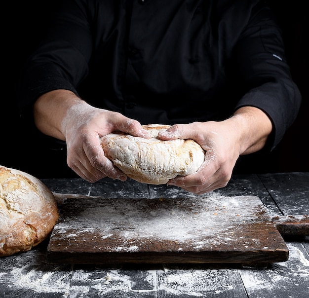 Male chef hands hold a whole loaf of baked round bread