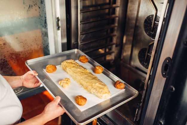 Photo male chef hands puts apple strudel on metal baking sheet in the oven. sweet bakery, dessert preparation