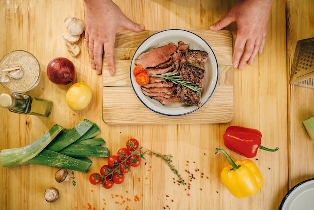 Mani di chef maschio e fette di carne arrosto in un piatto