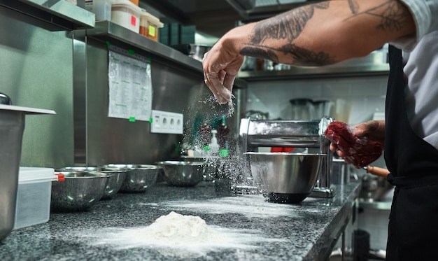 male chef hands with black tattoos pouring flour on kitchen table. food concept