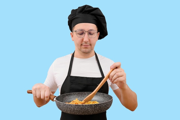 Male chef holding a frying pan prepares food on a blue background cooking and people concept