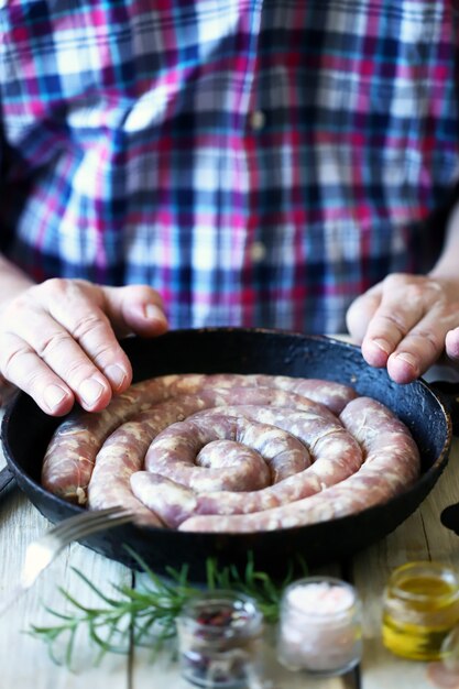 Шеф-повар кладет сырые сосиски в сковороду.