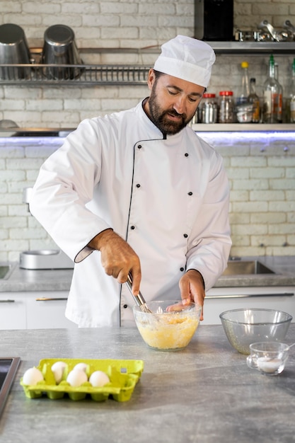 Foto cuoco unico maschio in cucina usando le uova per cucinare