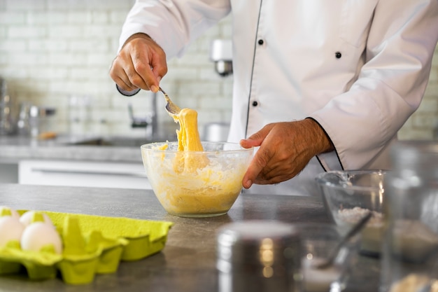 Foto cuoco unico maschio in cucina usando le uova per cucinare