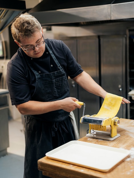 Foto cuoco unico maschio che rotola la pasta della pasta in cucina