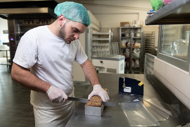 Chef maschio che affetta il pane sulla scatola di metallo della cucina