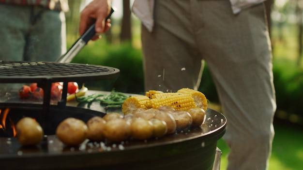 Male chef using forceps for cooking food outdoors Man hands pouring salt on bbq