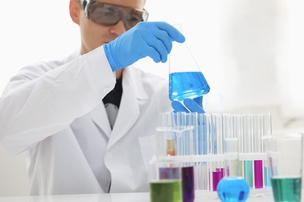 남성 화학자가 유리 시험관을 손에 들고 과망간산 칼륨의 액체 용액이 넘쳐 분석 반응을 수행합니다