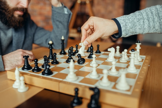 写真 ボードで遊んでいる男性のチェスプレーヤー、白い騎士がポーンを取ります。 2人のチェスプレイヤーが屋内で知的トーナメントを開始します。木製のテーブルの上のチェス盤
