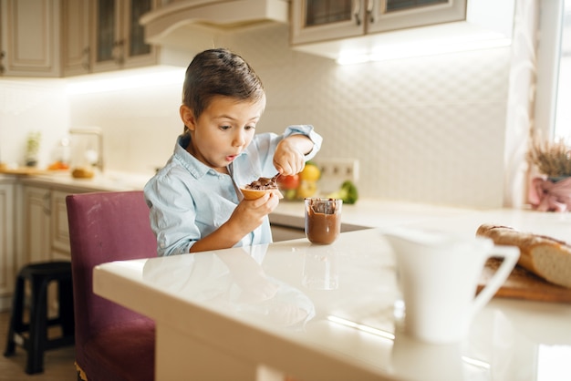 Male child smears melted chocolate on bread.