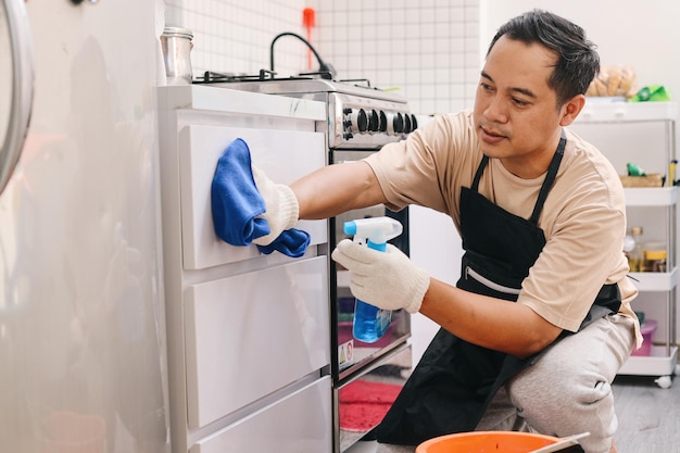 Мужчина чистит кухонные шкафы с помощью распылителя моющего средства и ткани