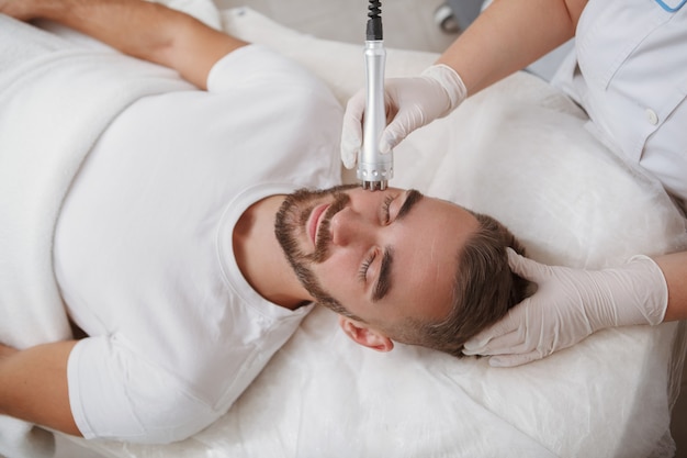 Male client getting rf-lifting facial treatment at cosmetology clinic