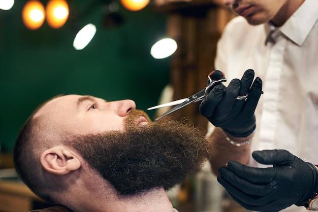 Male client with beard sitting in hairdresser chair Serious man with long brown beard Modern popular lumberjack style