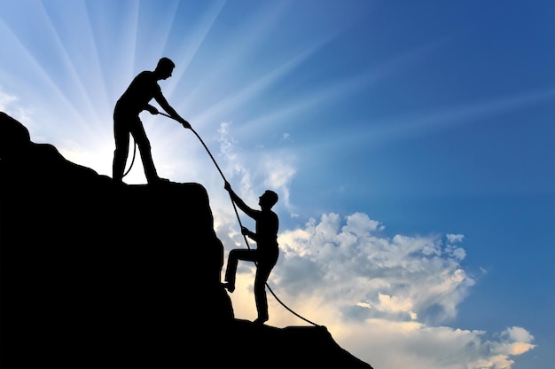 A male climber helps to climb the top of another person by throwing him a rope. Conceptual Scene