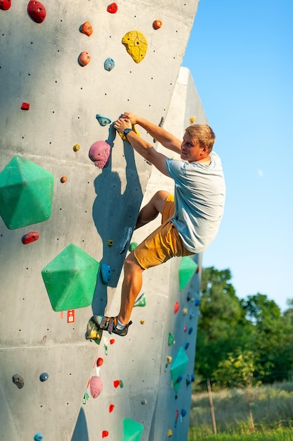 A male climber is rock climbing outdoors on an artificial boulder without a safety harness