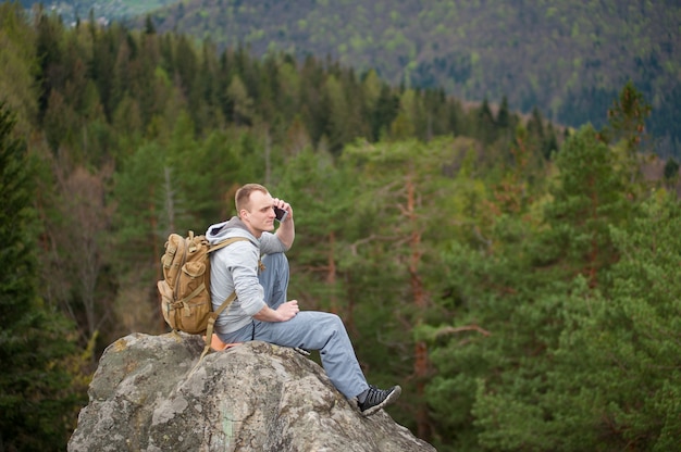 Male climber with brown backpack on the peak of rock