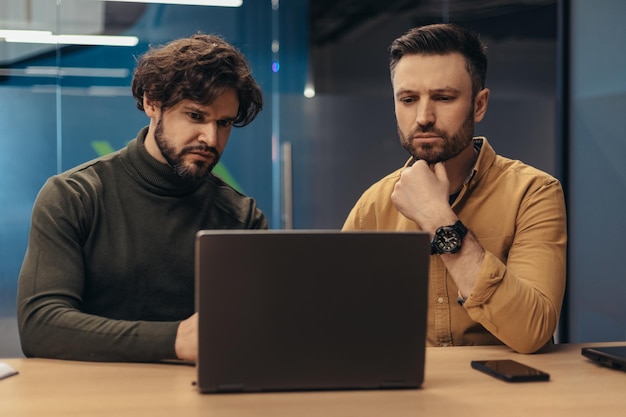 Male colleagues working on business project looking at laptop screen thinking over development