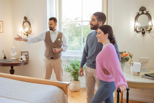 Foto concierge maschile che mostra ai turisti la loro camera in hotel al chiuso