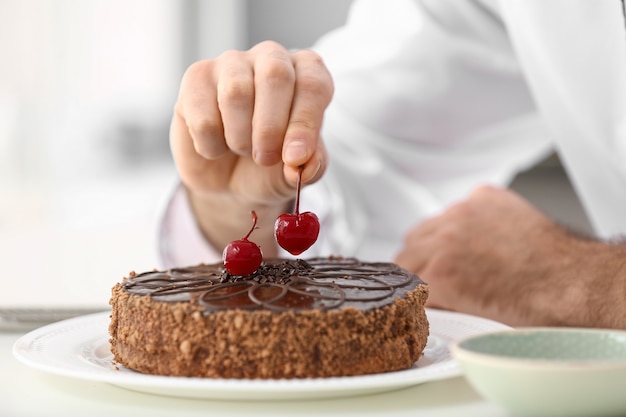 Foto pasticcere maschio che decora una gustosa torta al cioccolato in cucina