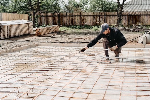 男性の建設労働者は、コンクリートを注いで家の建設の基礎のために金具を設置します